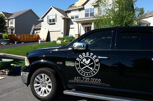 Rooster Exteriors company truck working on a residential roof in the background